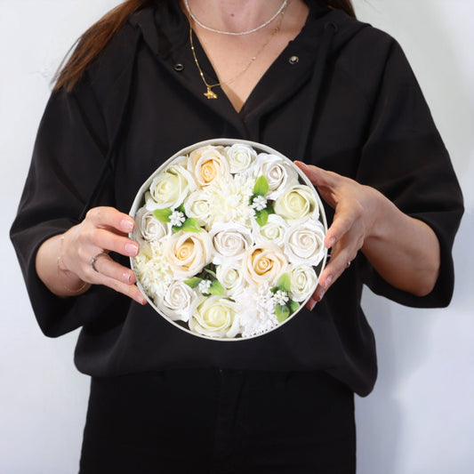 Persona sosteniendo una caja redonda con flores de jabón blancas y marfil, estilo elegante para regalo de bodas.