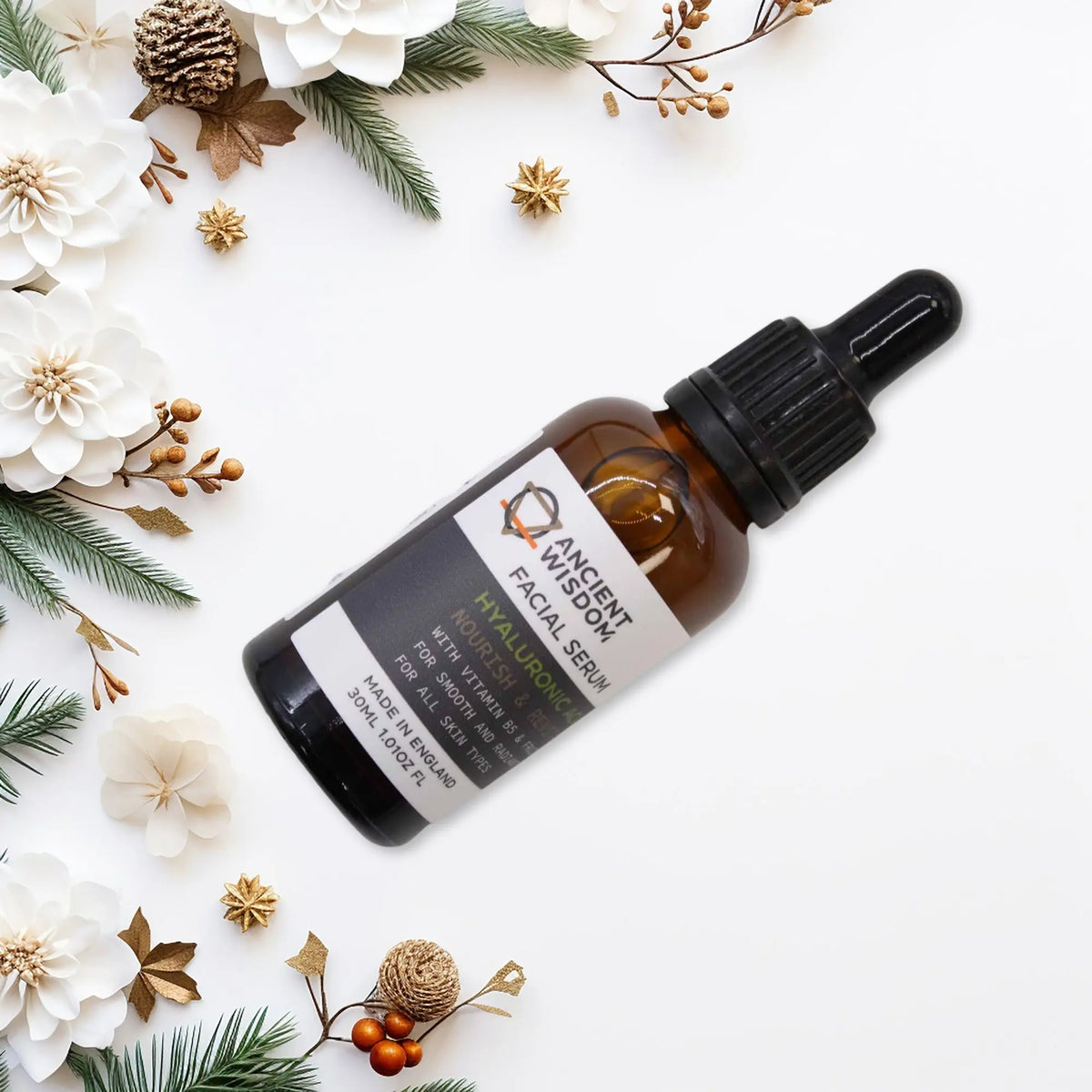 Serum facial Ancient Wisdom en frasco ámbar con gotero, sobre fondo blanco decorado con flores y motivos navideños.
