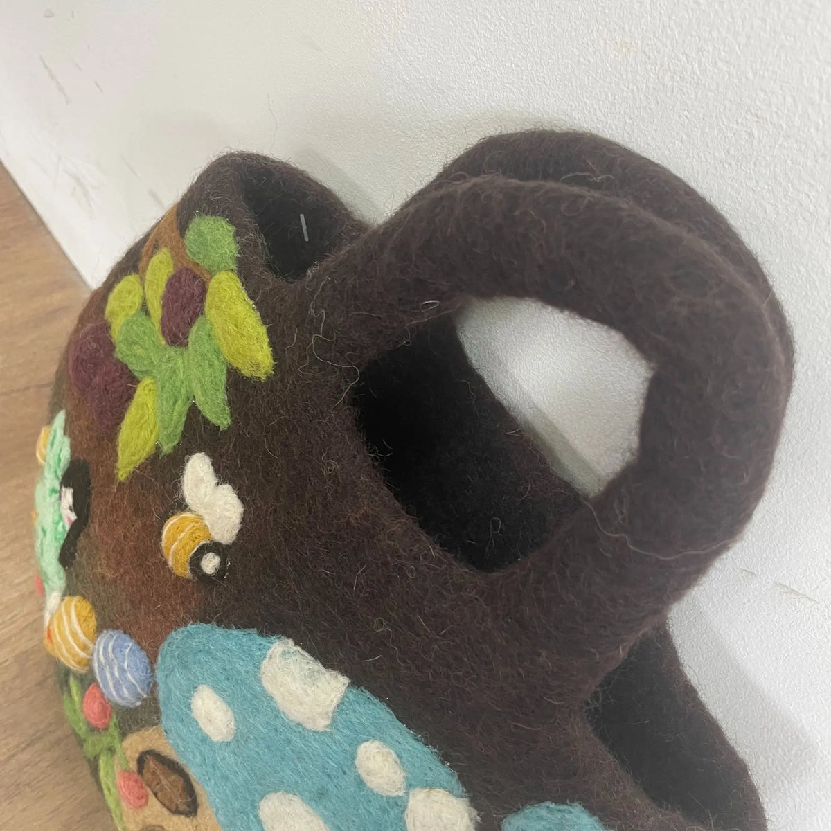 Bolsa de fieltro marrón con decoraciones de jardín, flores, setas y abejas en colores vivos. Estilo artesanal.
