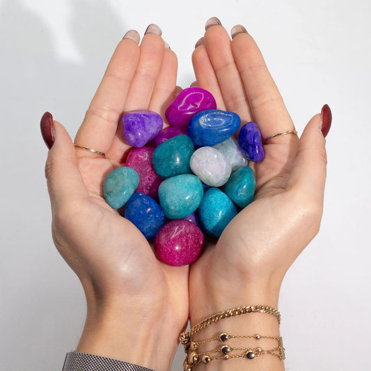 Piedras de colores vibrantes en tonos púrpura, verde y azul, sostenidas en manos delicadas.