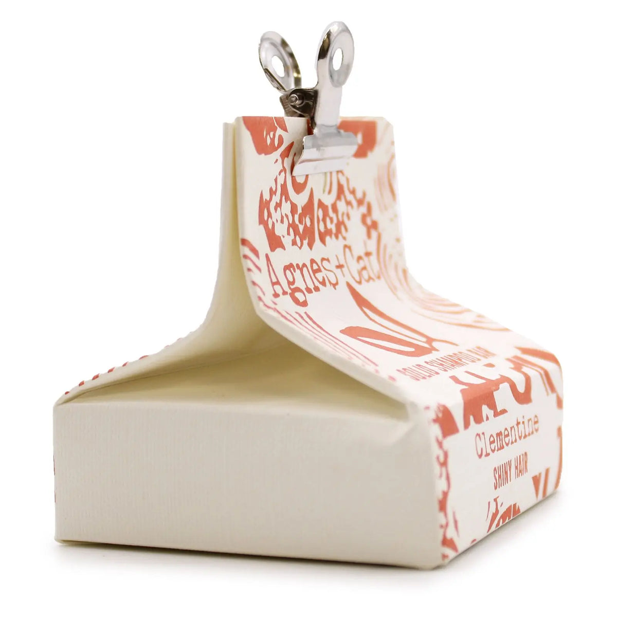 Champú sólido Agnes+Cat aroma clementina en envoltorio de papel blanco con diseño naranja y pinza metálica superior.