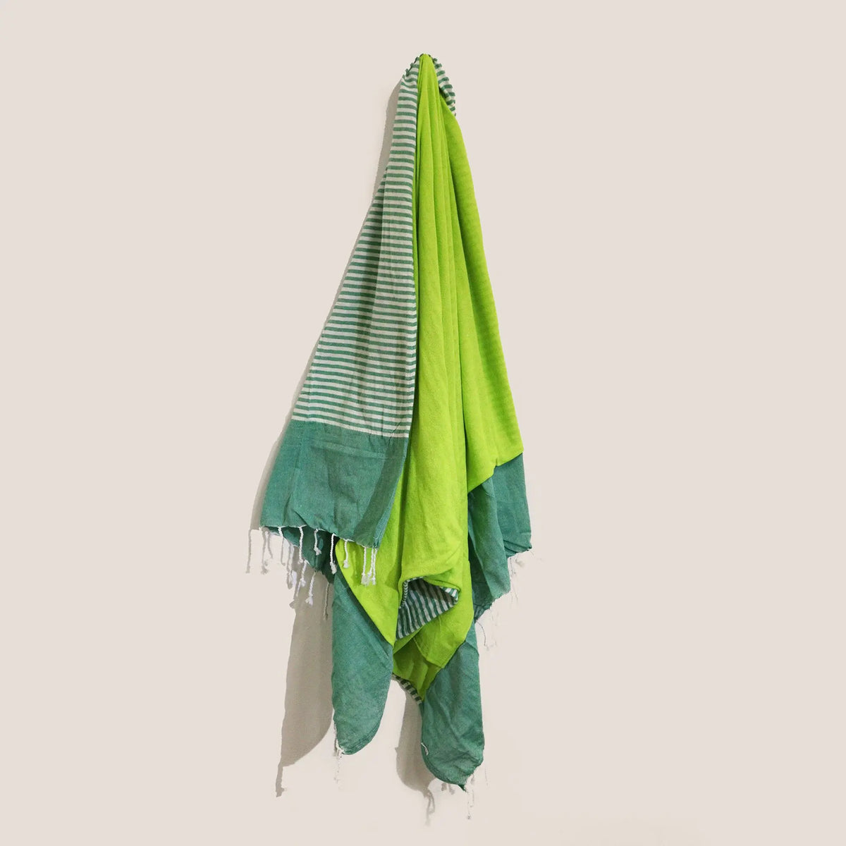 Toalla pareo de algodón verde con rayas y flecos, colgada verticalmente. Textura suave, estilo veraniego y casual.