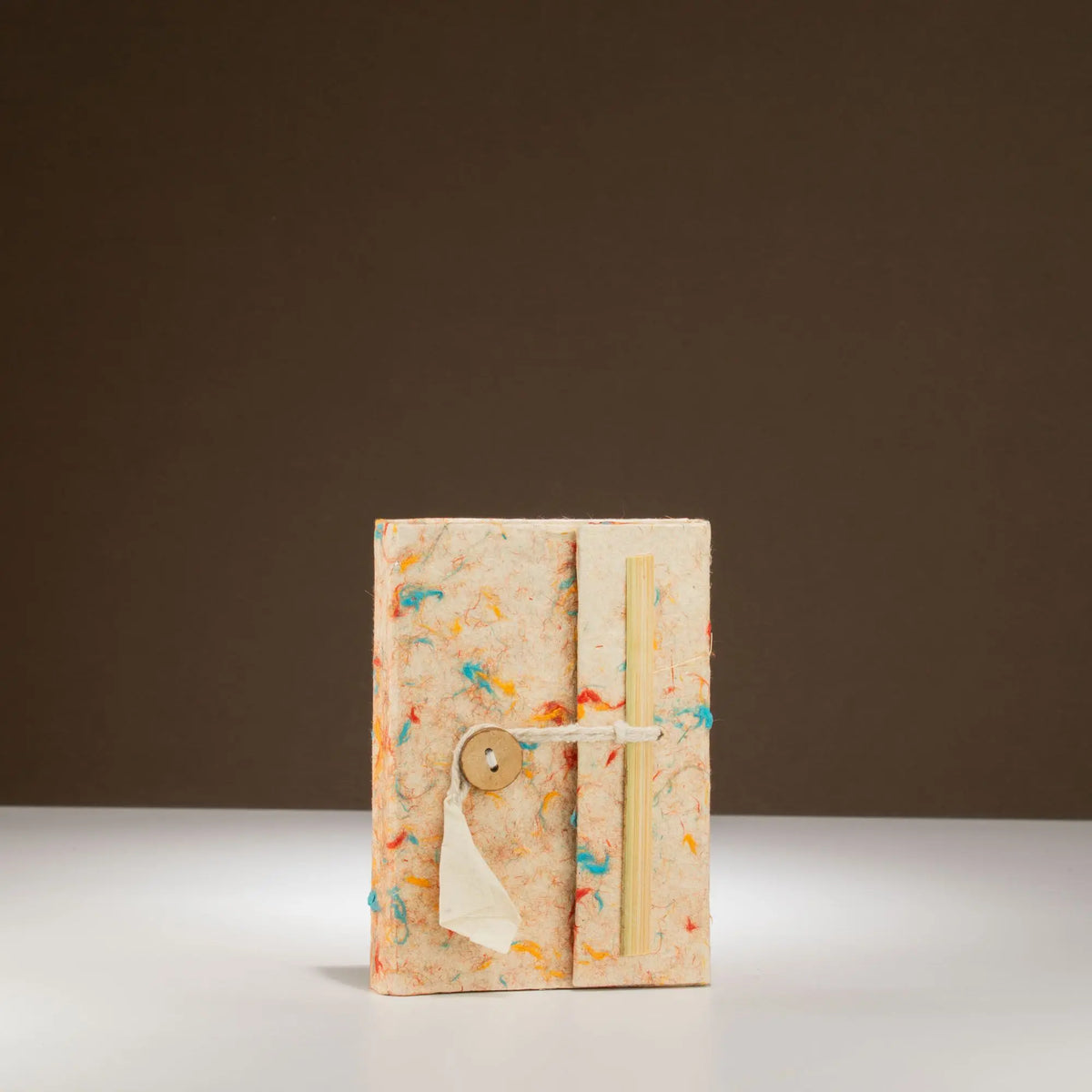 Cuaderno artesanal con tapa de papel reciclado en tonos beige y detalles de colores, cierre con botón de madera.