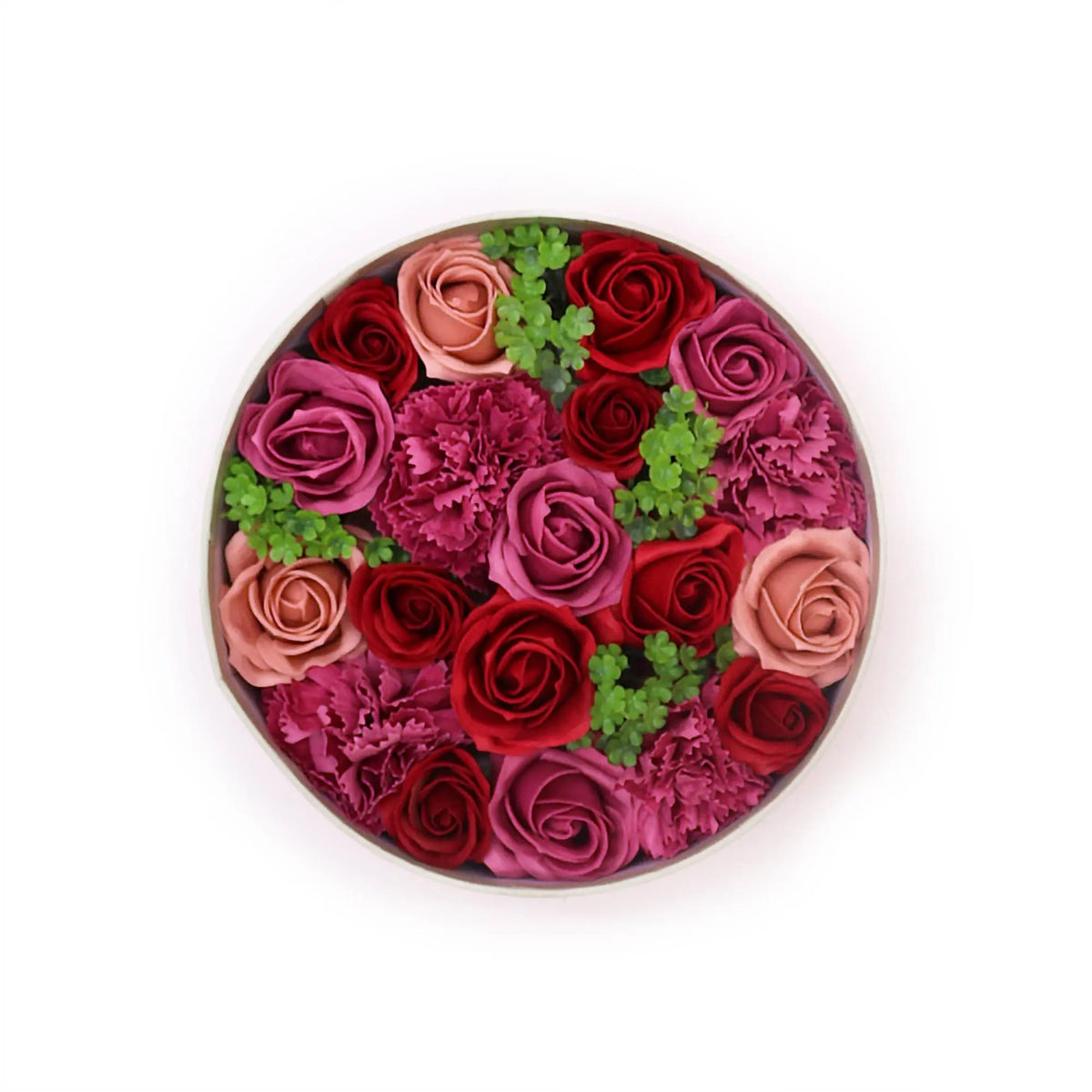 Caja redonda con arreglo de rosas y claveles de jabón en tonos rojos, rosas y nude, decorado con pequeñas hojas verdes.