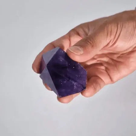 Cristal de amatista morado en mano, forma geométrica, superficie lisa, ideal para decoración y meditación.
