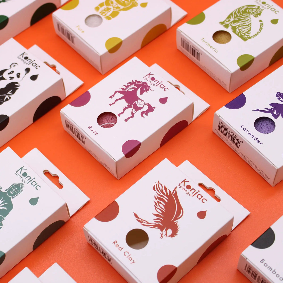 Cajas de esponjas faciales Konjac de colores sobre fondo naranja. Destaca el empaque de arcilla roja con un fénix.