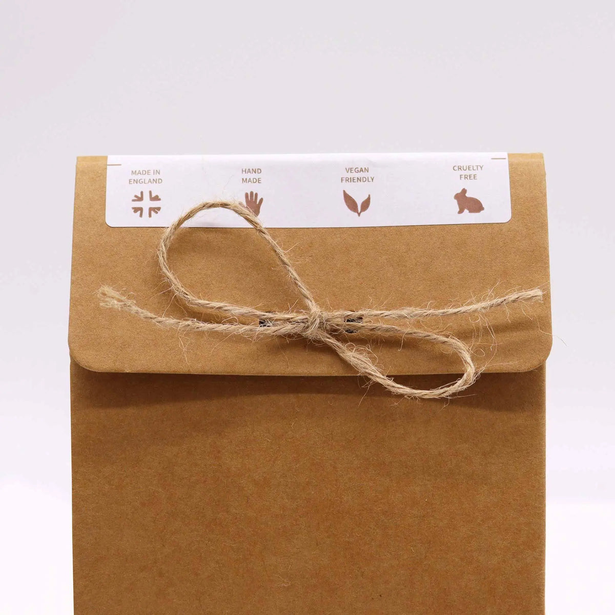 Bolsa de papel kraft cerrada con cuerda, etiqueta con iconos de fabricación artesanal, vegana y libre de crueldad.