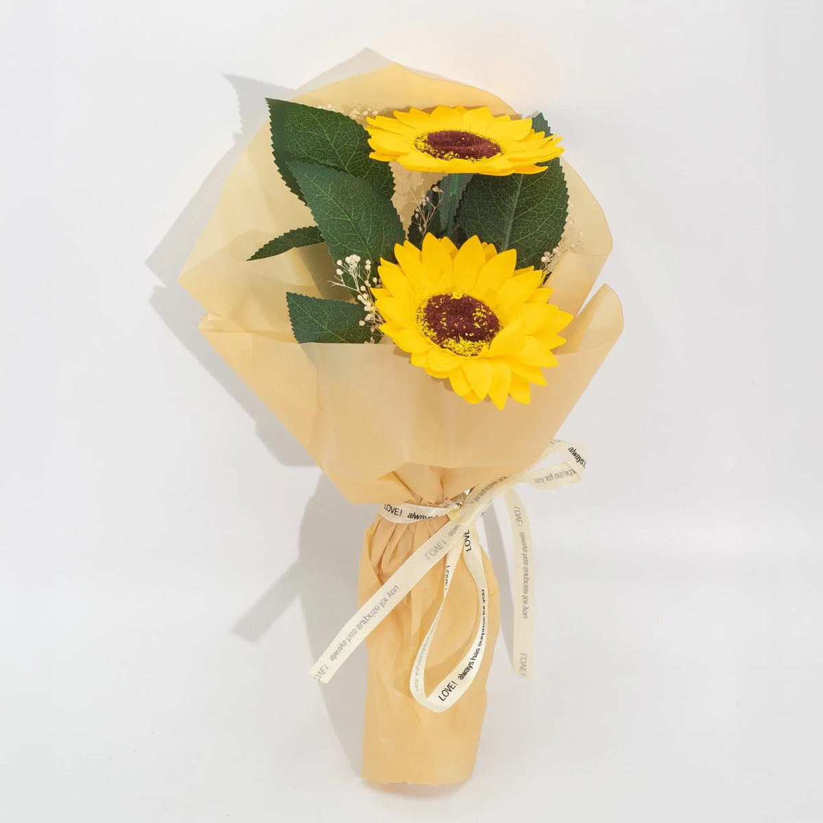 Ramo de regalo con dos girasoles de jabón amarillo brillante, hojas verdes y papel envoltorio beige con cinta decorativa.