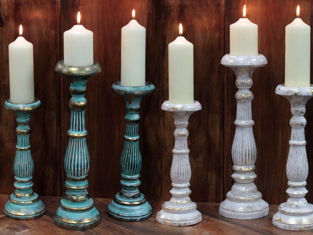 Candelabros de madera torneada estilo vintage en colores azul y blanco con detalles dorados, portando velas blancas.