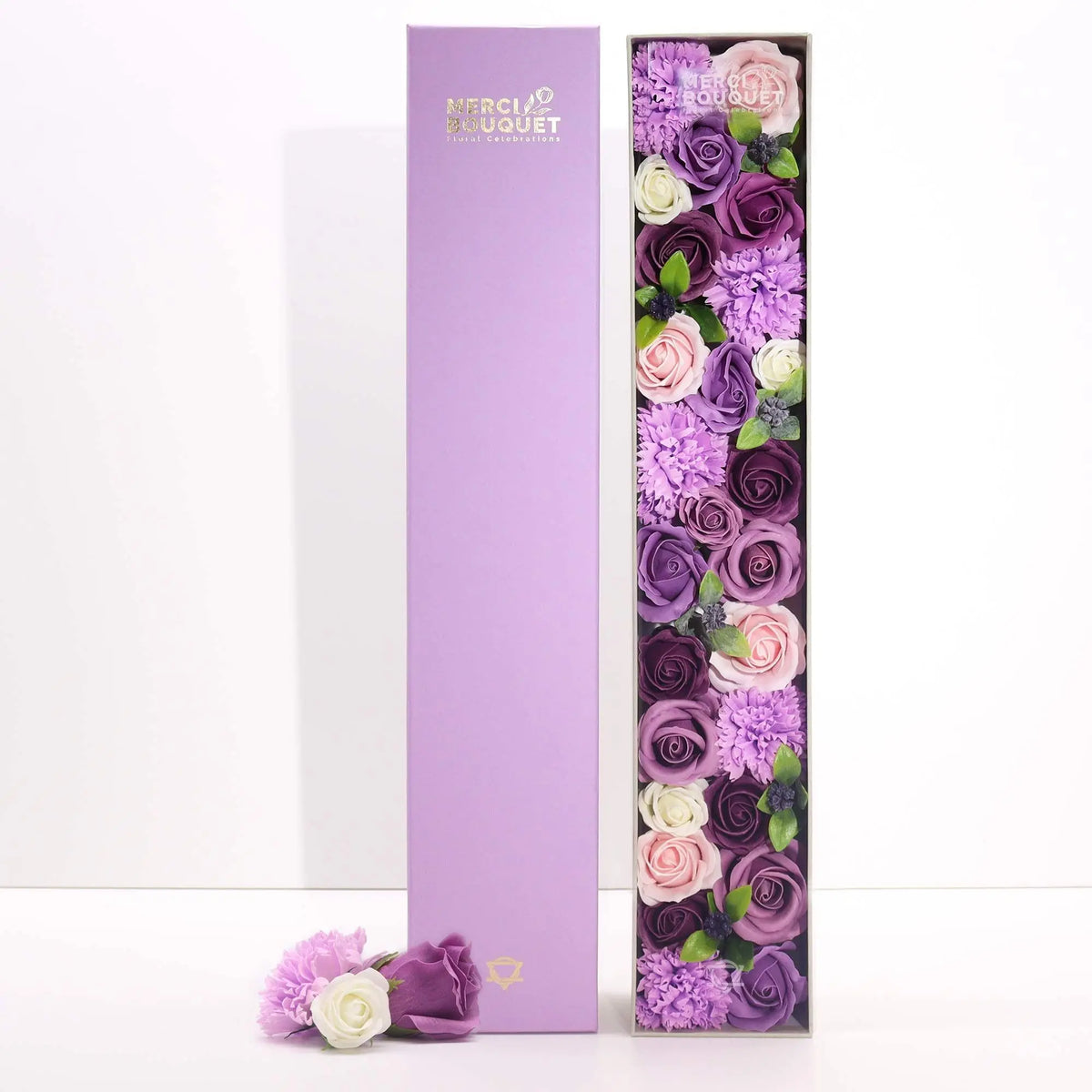 Caja rectangular alta con flores de jabón en tonos morado, rosa y blanco, con rosas y claveles decorativos.