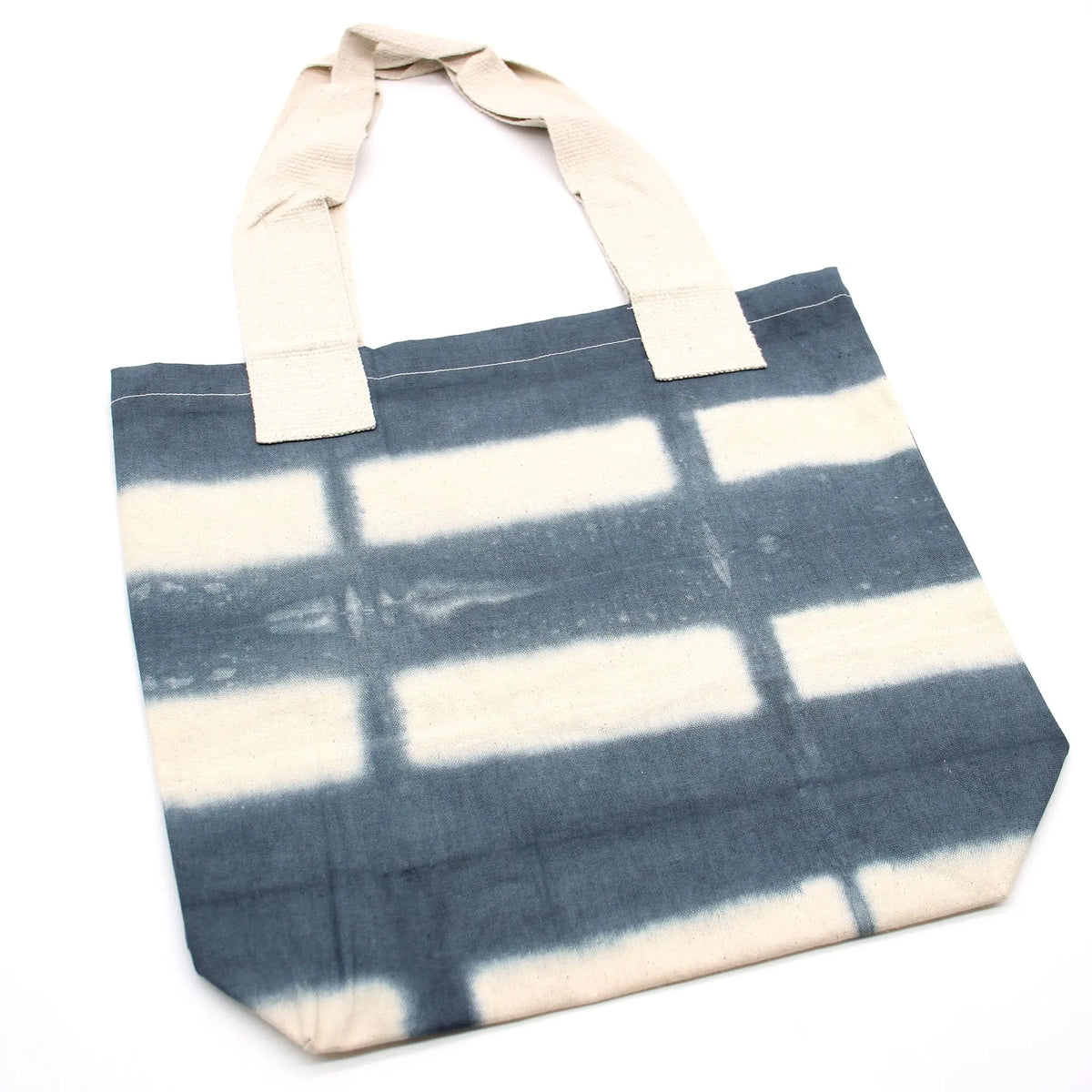 Bolsa de algodón natural con estampado tie-dye de rectángulos grises y asas color crema sobre fondo blanco.