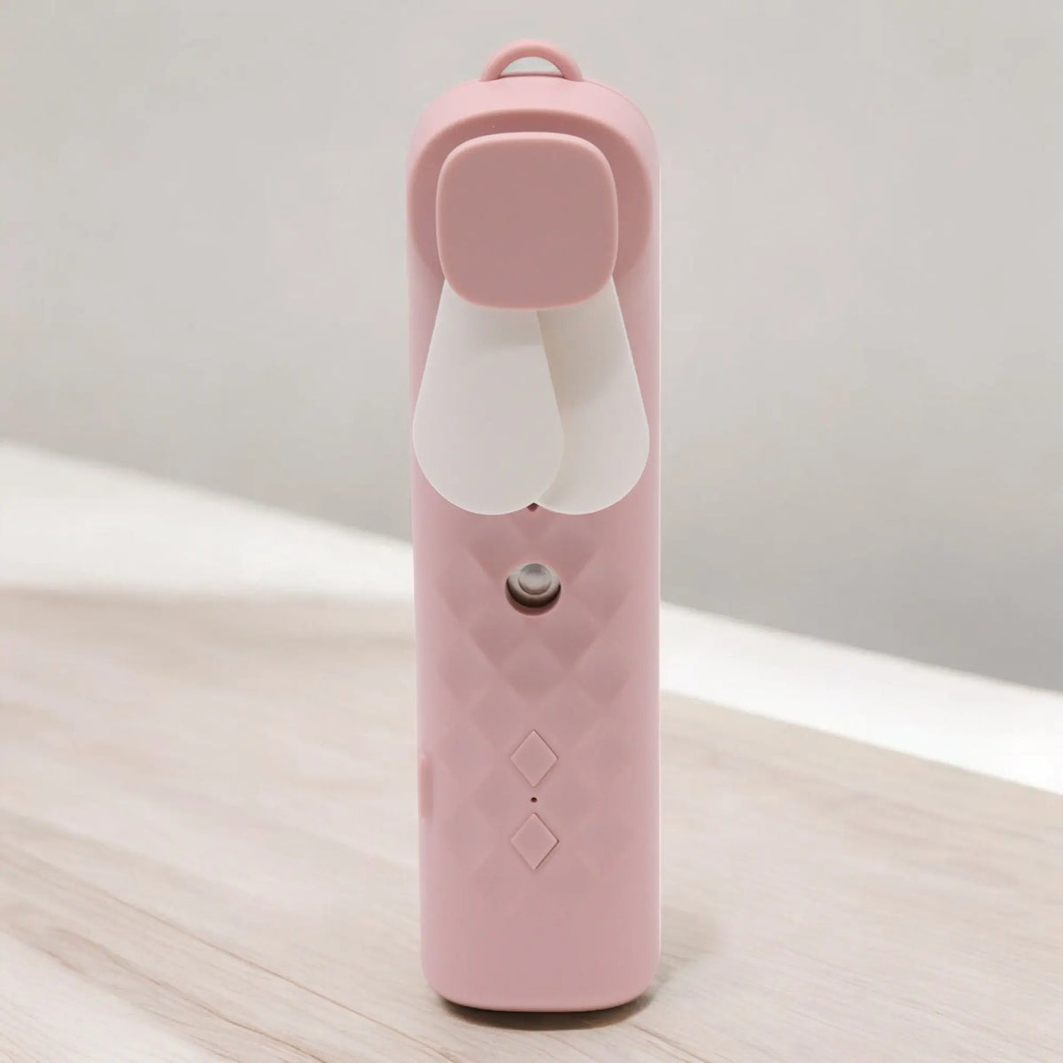Ventilador pulverizador facial rosa, diseño cilíndrico con textura de rombos, aspas blancas y botones frontales.