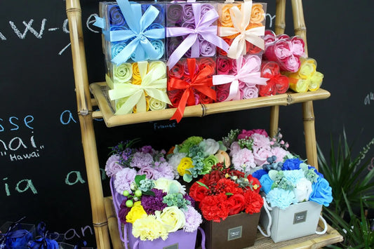 Cajas de regalo con flores de jabón de diversos colores y estilos exhibidas sobre un estante de bambú decorativo