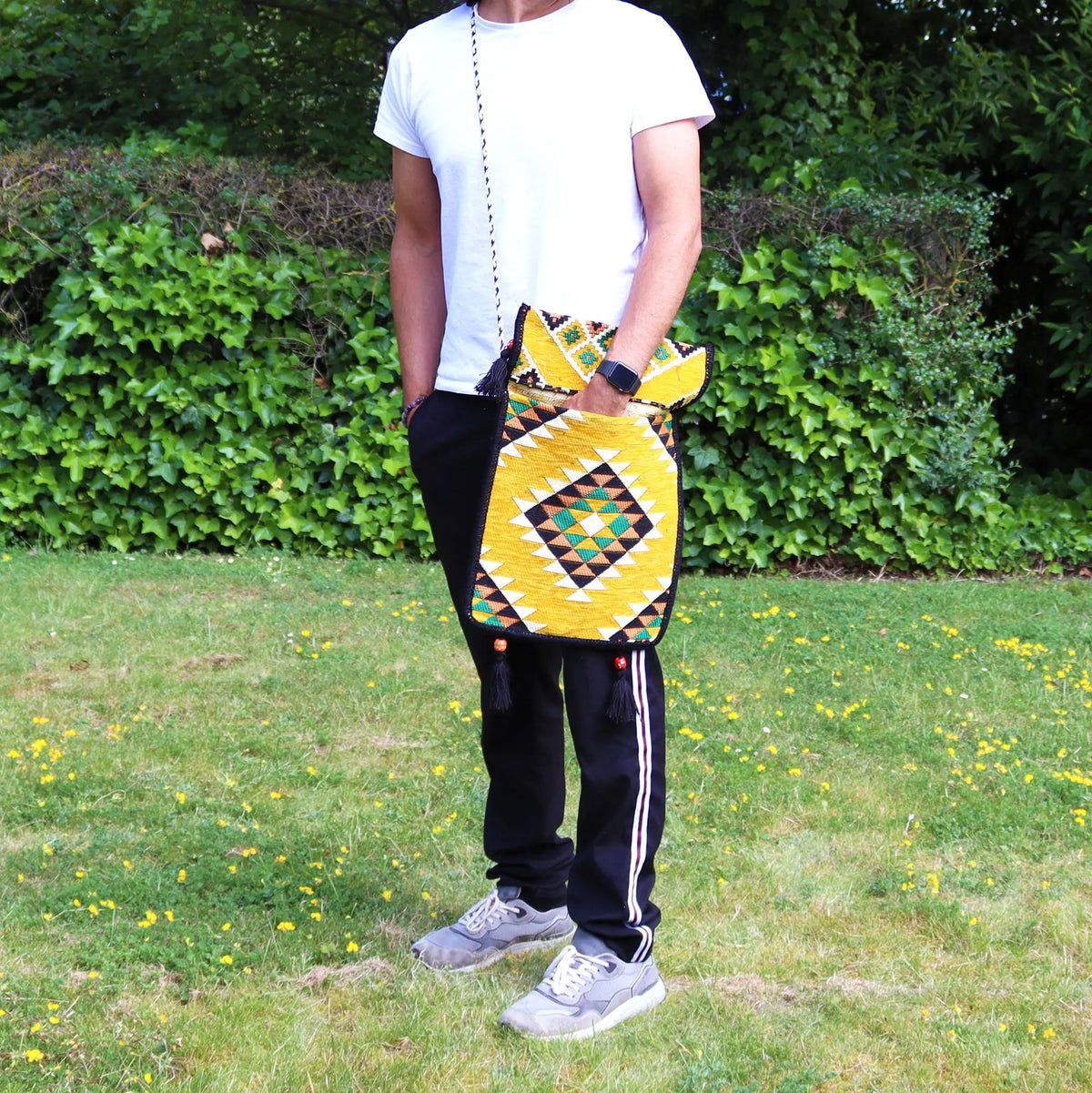 Bolso messenger de tela kilim amarilla con patrón geométrico, solapa y borlas, usado cruzado en exterior.