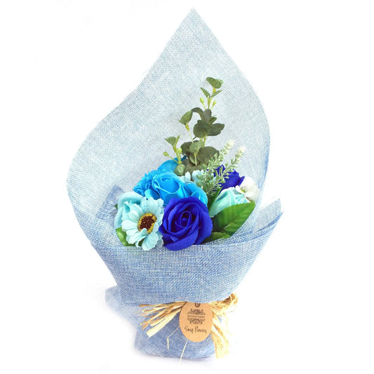 Ramo de flores de jabón en tonos azules, envuelto en tela tipo arpillera azul con lazo de rafia, fondo blanco.
