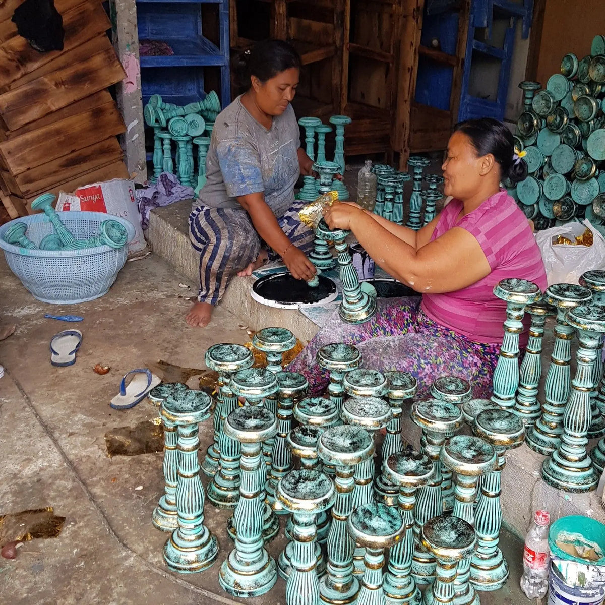 Dos mujeres elaboran candelabros de madera vintage en acabado rústico verde con bordes dorados, de estilo artesanal.