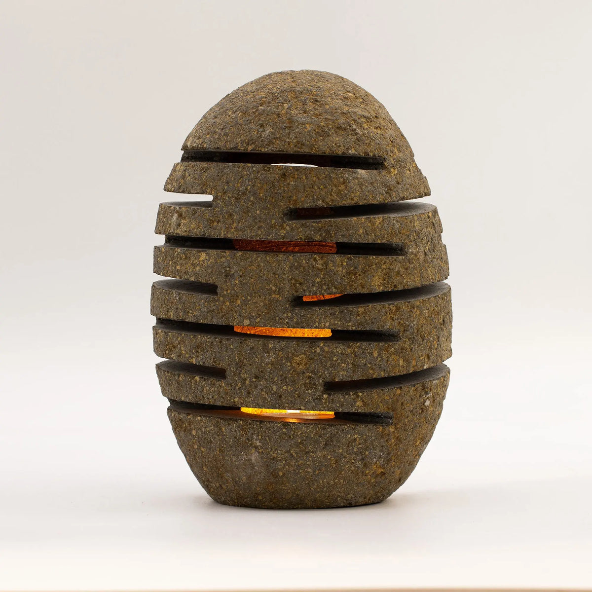 Lámpara decorativa de piedra gris, estilo moderno, con ranuras que emiten luz cálida. Ideal para interior.