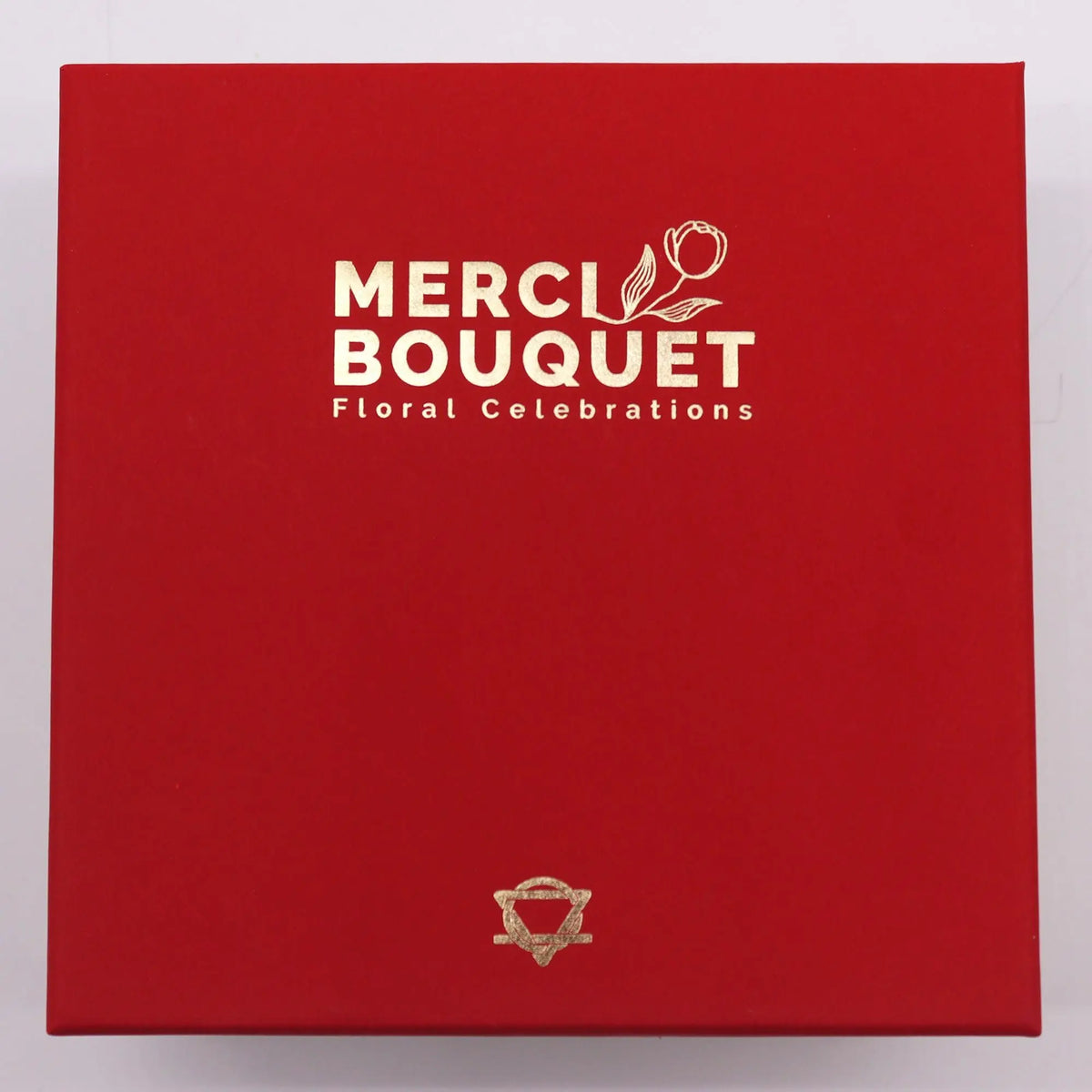 Caja de regalo cuadrada en color rojo intenso, con detalles en letras y símbolos de color dorado.