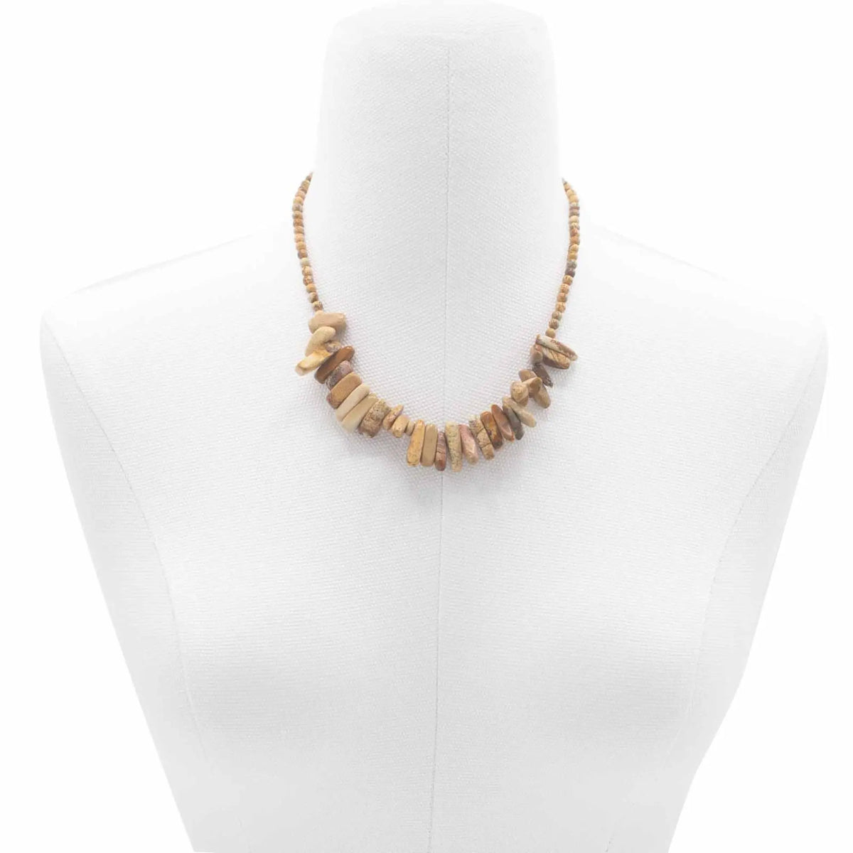 Collar de piedras naturales en tonos tierra con forma irregular, sobre busto de maniquí blanco.