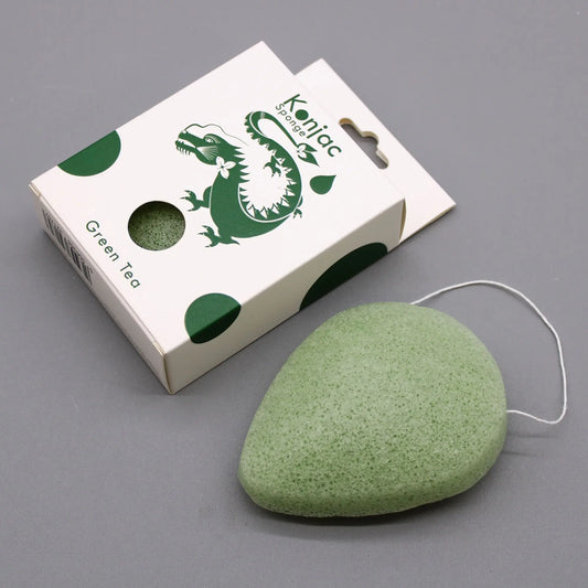 Esponja facial de konjac verde, forma de gota, con hilo colgante junto a su caja de cartón blanca con diseño de dragón.