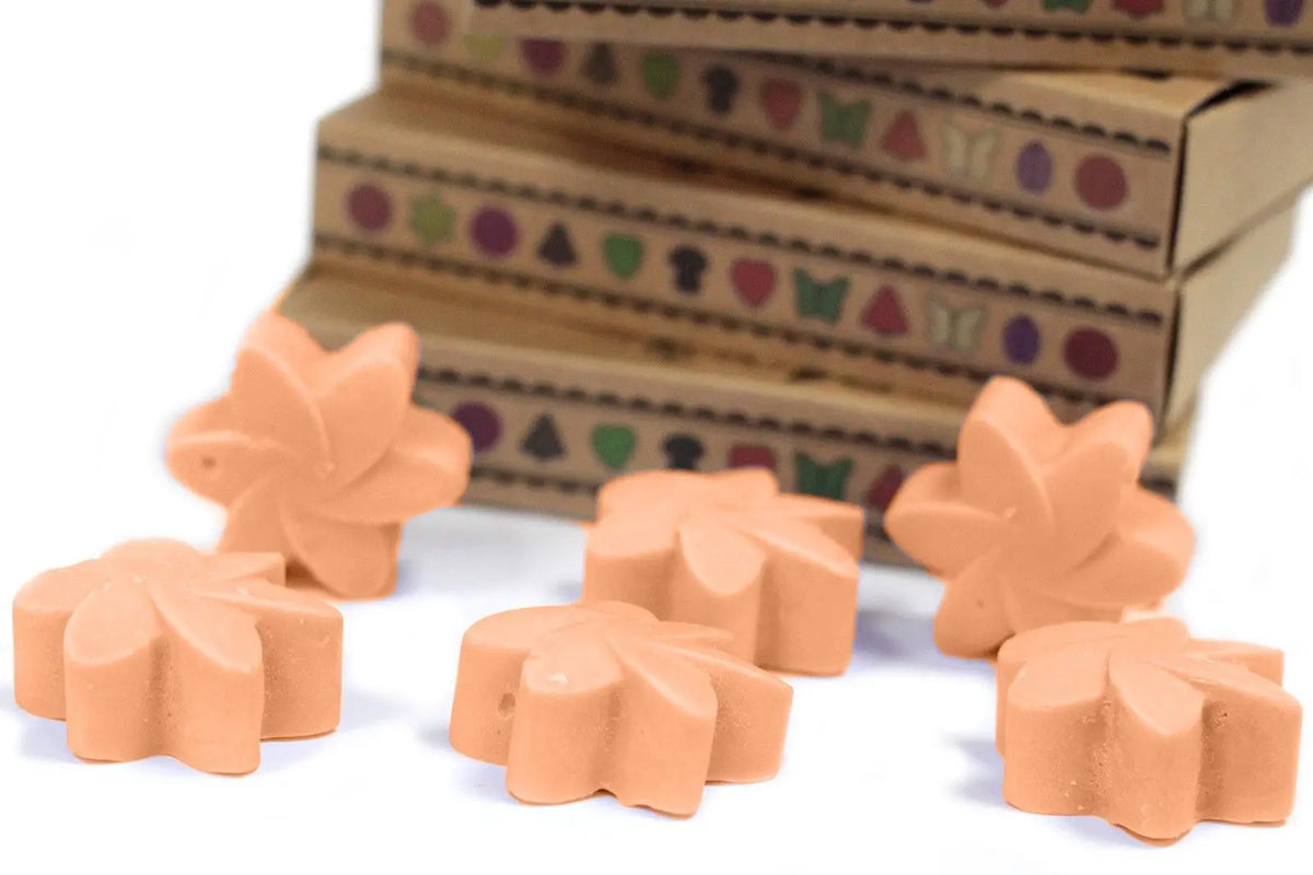 Seis piezas de cera de soja color melocotón en forma de flor frente a cajas de regalo apiladas de cartón kraft.