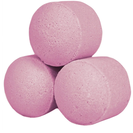 Tres mini bombas de baño efervescentes de color rosa con forma cilíndrica y textura porosa sobre fondo blanco.