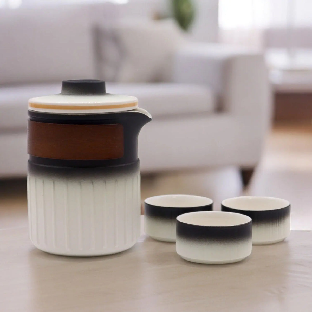 Juego de té de cerámica con tetera cilíndrica y tres tazas, en degradado de blanco a negro y detalle de madera.