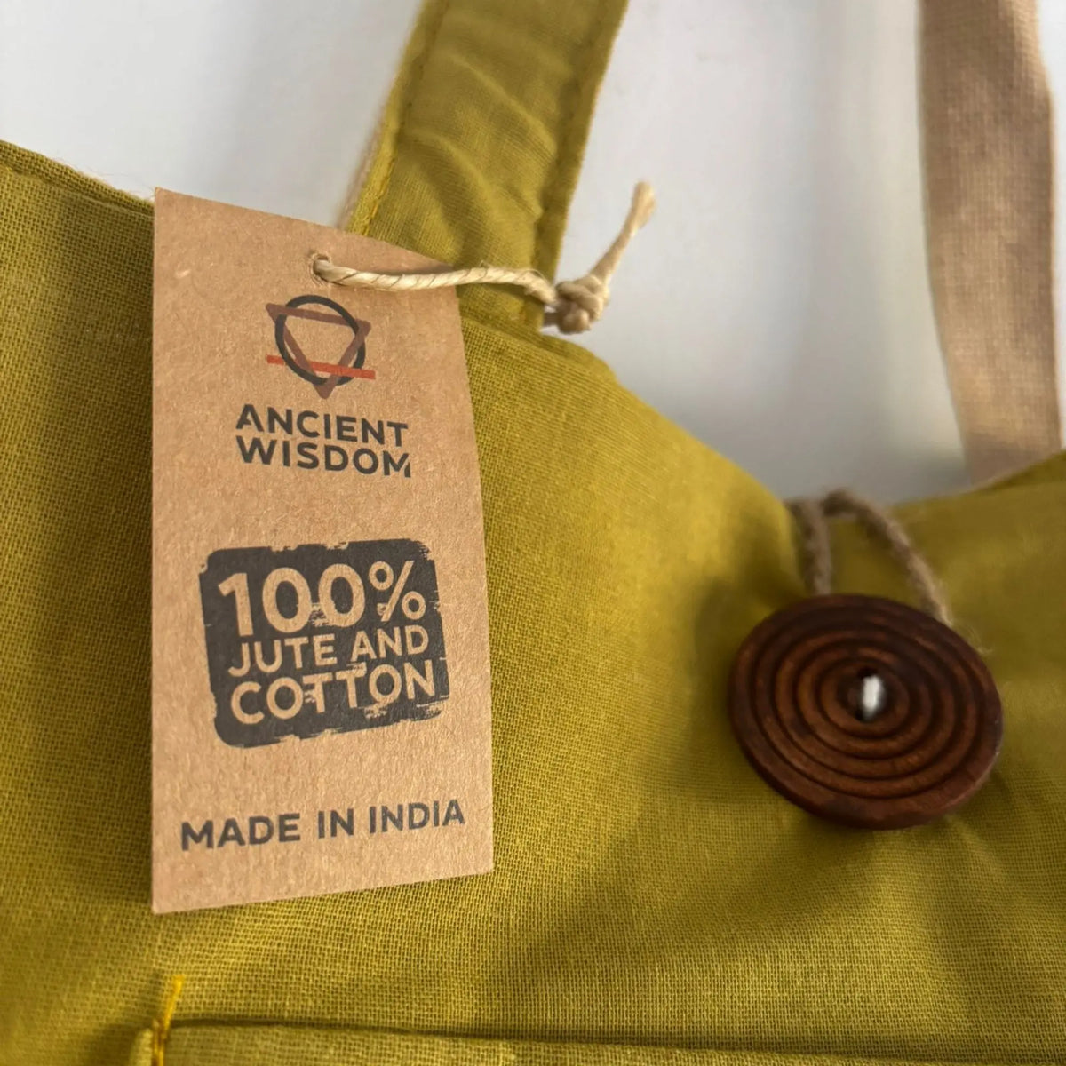 Bolsa grande color pistacho de yute y algodón con botón de madera decorativo y etiqueta de producto colgante.
