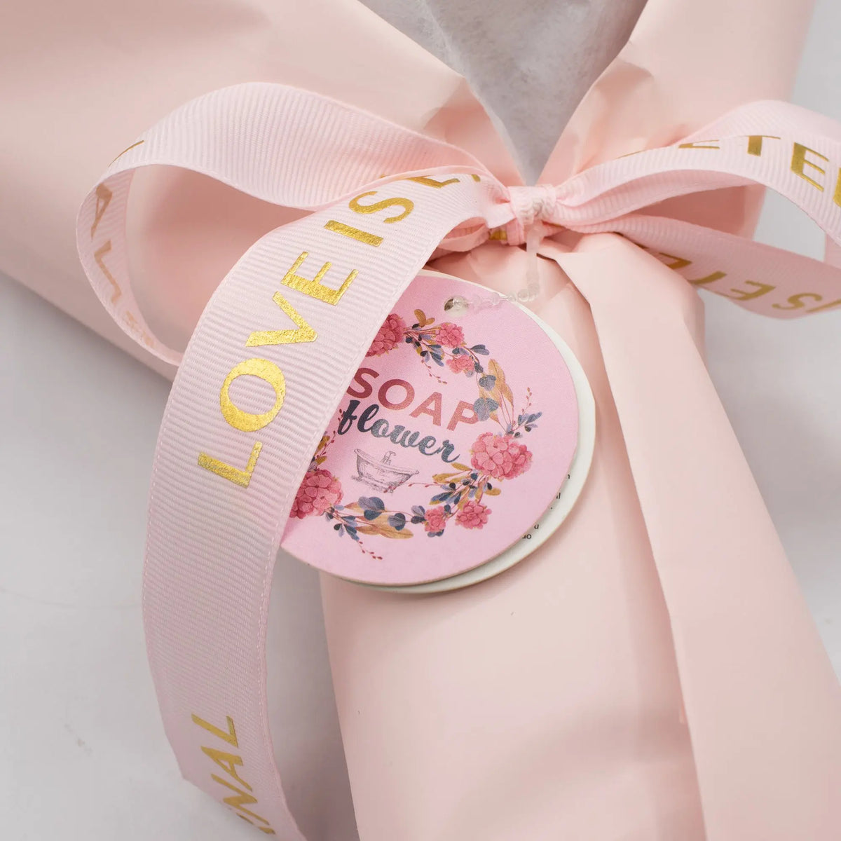 Ramo de flores de jabón en papel rosa con cinta dorada, etiqueta decorativa, estilo elegante y romántico.