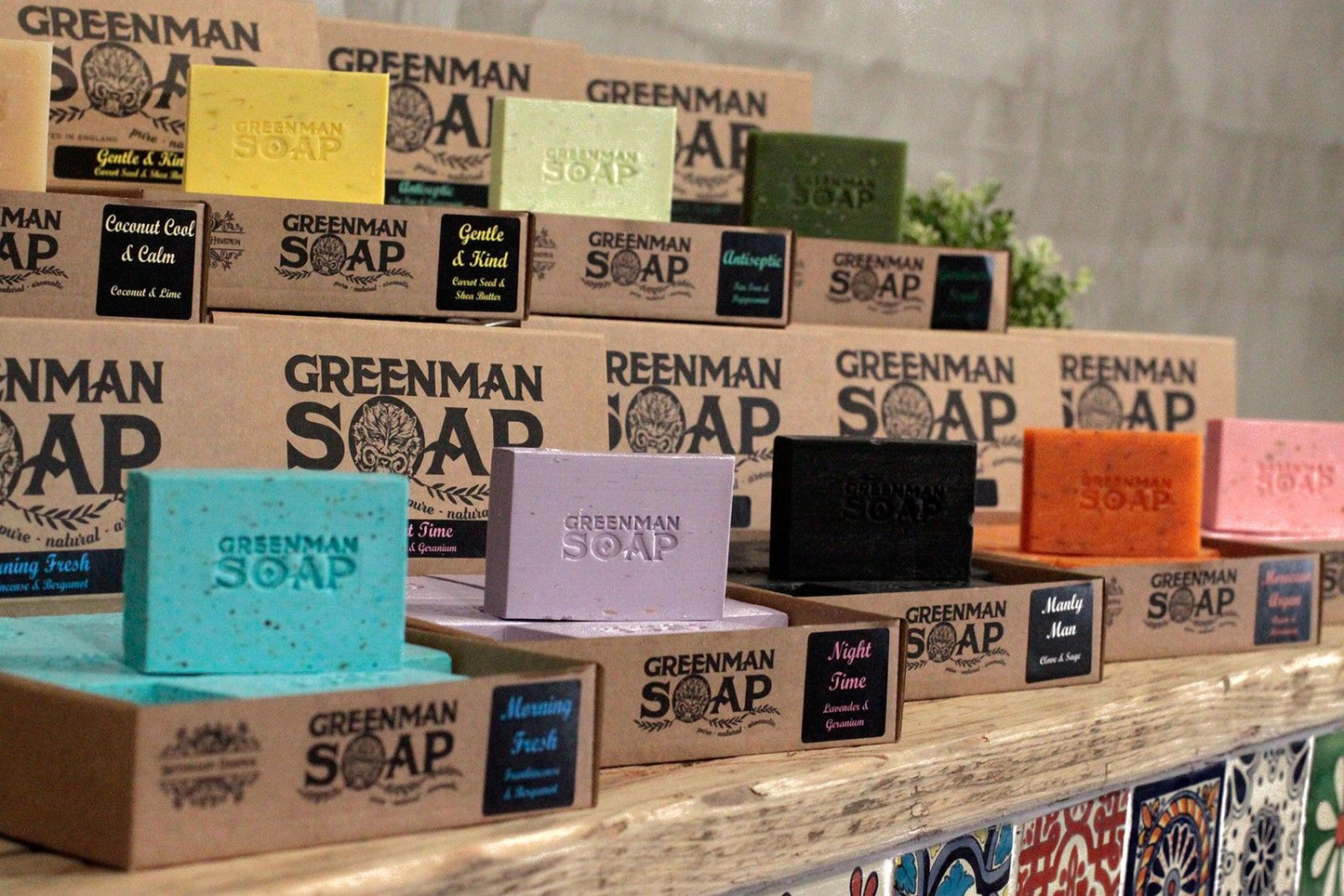 Exhibición de jabones artesanales Greenman en cajas de cartón; destaca el jabón azul "Mañana fresca" en primer plano.