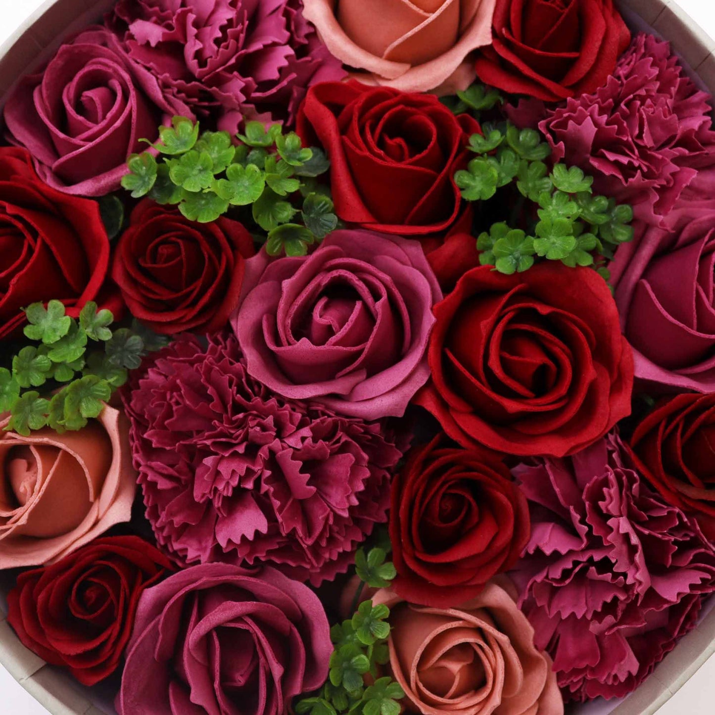 Caja redonda con rosas de jabón en tonos rojos, fucsia y rosa vintage, decoradas con pequeñas hojas verdes.