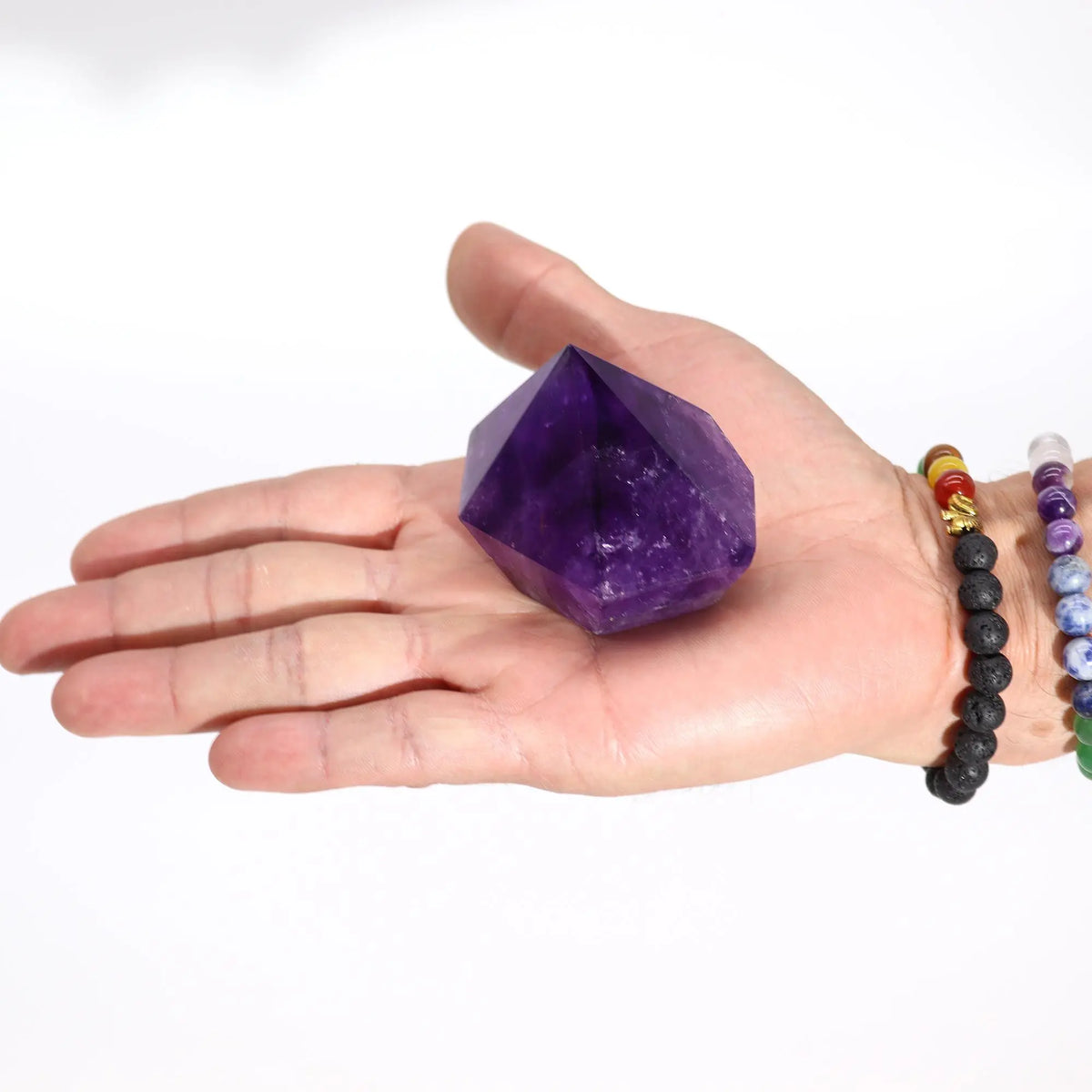 Cristal de amatista púrpura en forma de pirámide, sostenido en una mano. Ideal para decoración y energías positivas.