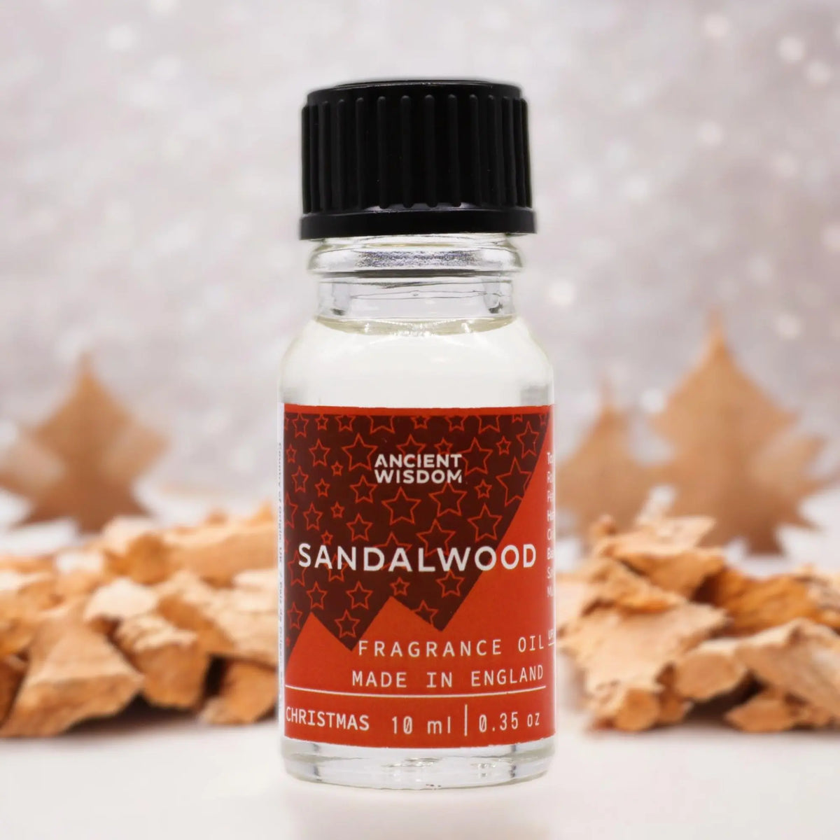 Frasco de 10ml de aceite de sándalo con etiqueta roja, tapa negra, sobre fondo de decoración navideña con madera.