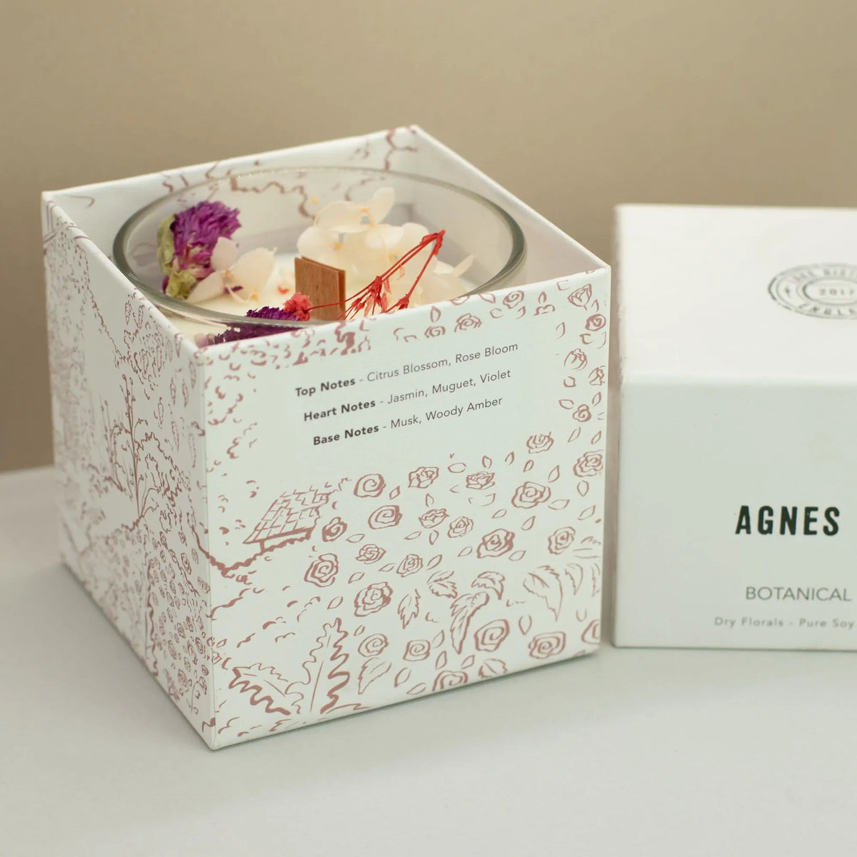 Vela aromática en caja blanca con diseño floral, notas de cítricos, jazmín y madera, ideal para decoración y relax.