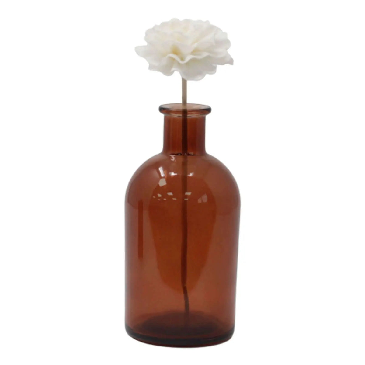 Flor difusora blanca sobre caña en frasco de vidrio ámbar cilíndrico sobre fondo blanco.