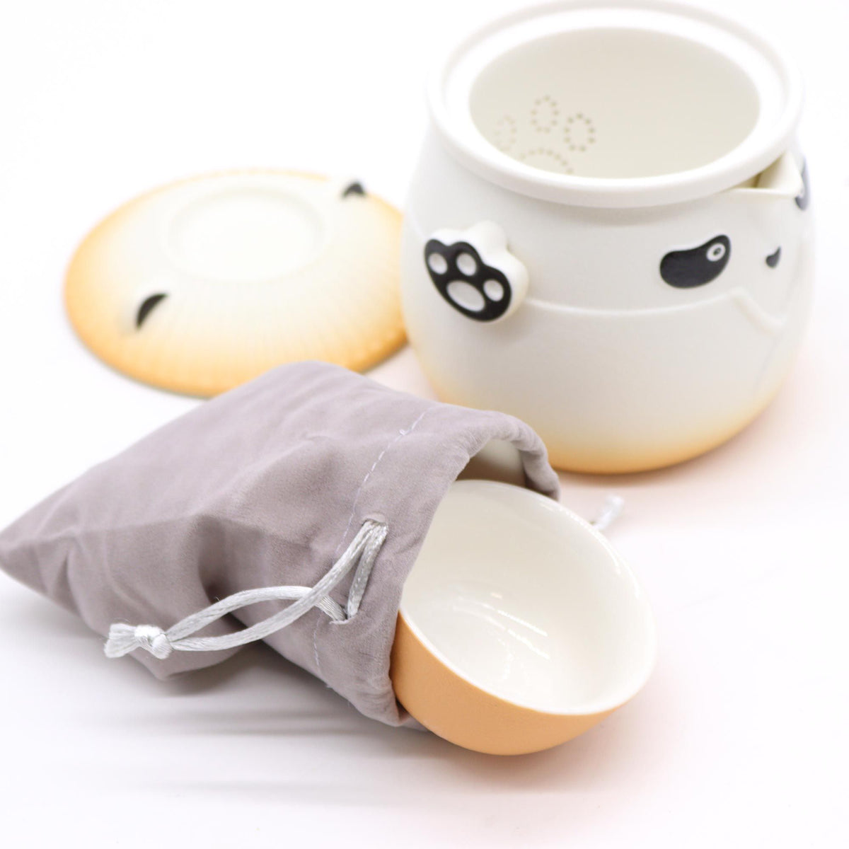 Juego de té de cerámica con diseño de panda, incluye tetera y taza naranja con detalles en blanco y bolsa de tela gris.