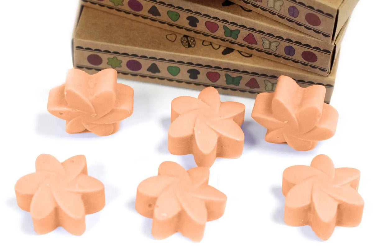 Seis ceras de soja color melocotón con forma de flor, frente a cajas de cartón decoradas con motivos naturales.