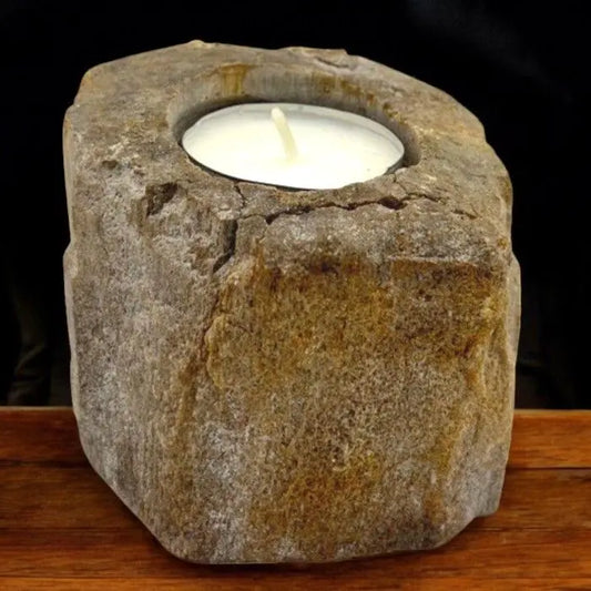 Portavelas bajo de madera petrificada con textura rugosa y tonos tierra, sosteniendo una vela de té blanca.