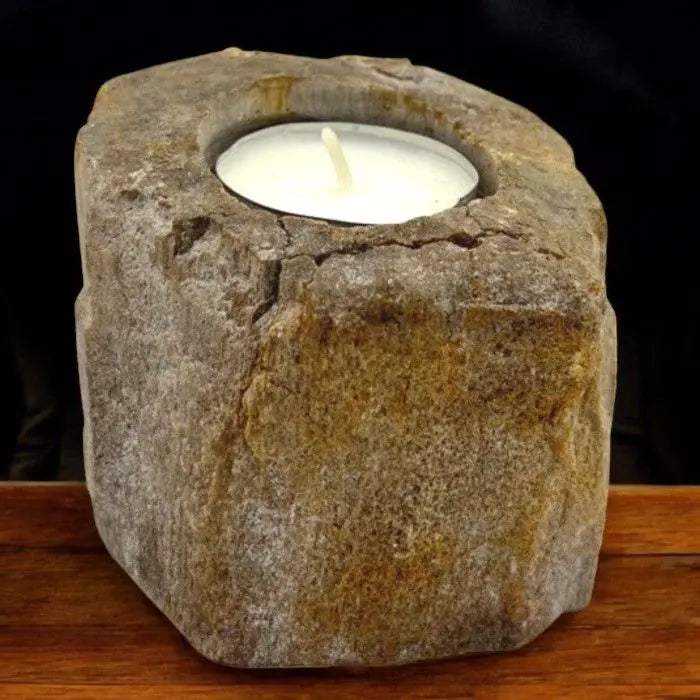 Portavelas bajo de madera petrificada con textura rugosa y tonos tierra, sosteniendo una vela de té blanca.