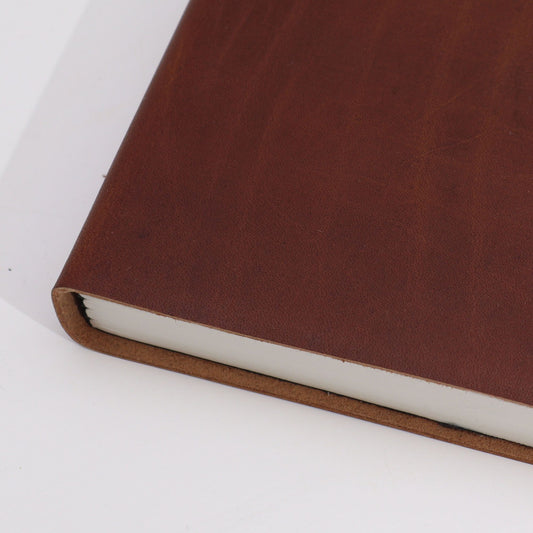 Cuaderno de tapa dura en cuero marrón oscuro con hojas blancas, estilo clásico y elegante, fondo blanco.