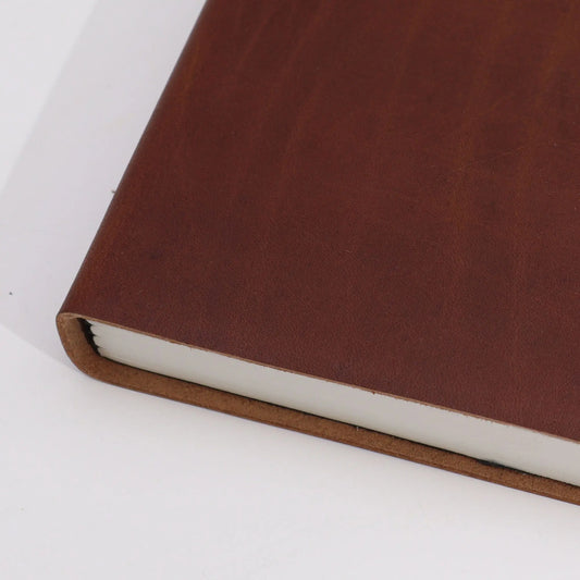Cuaderno de tapa dura en cuero marrón oscuro con hojas blancas, estilo clásico y elegante, fondo blanco.