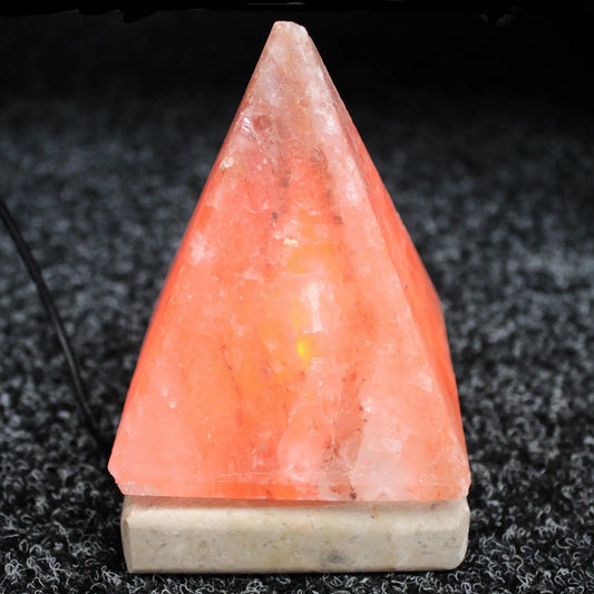 Lámpara de sal del Himalaya con forma de pirámide naranja sobre base cuadrada de piedra, fondo oscuro, conexión USB.