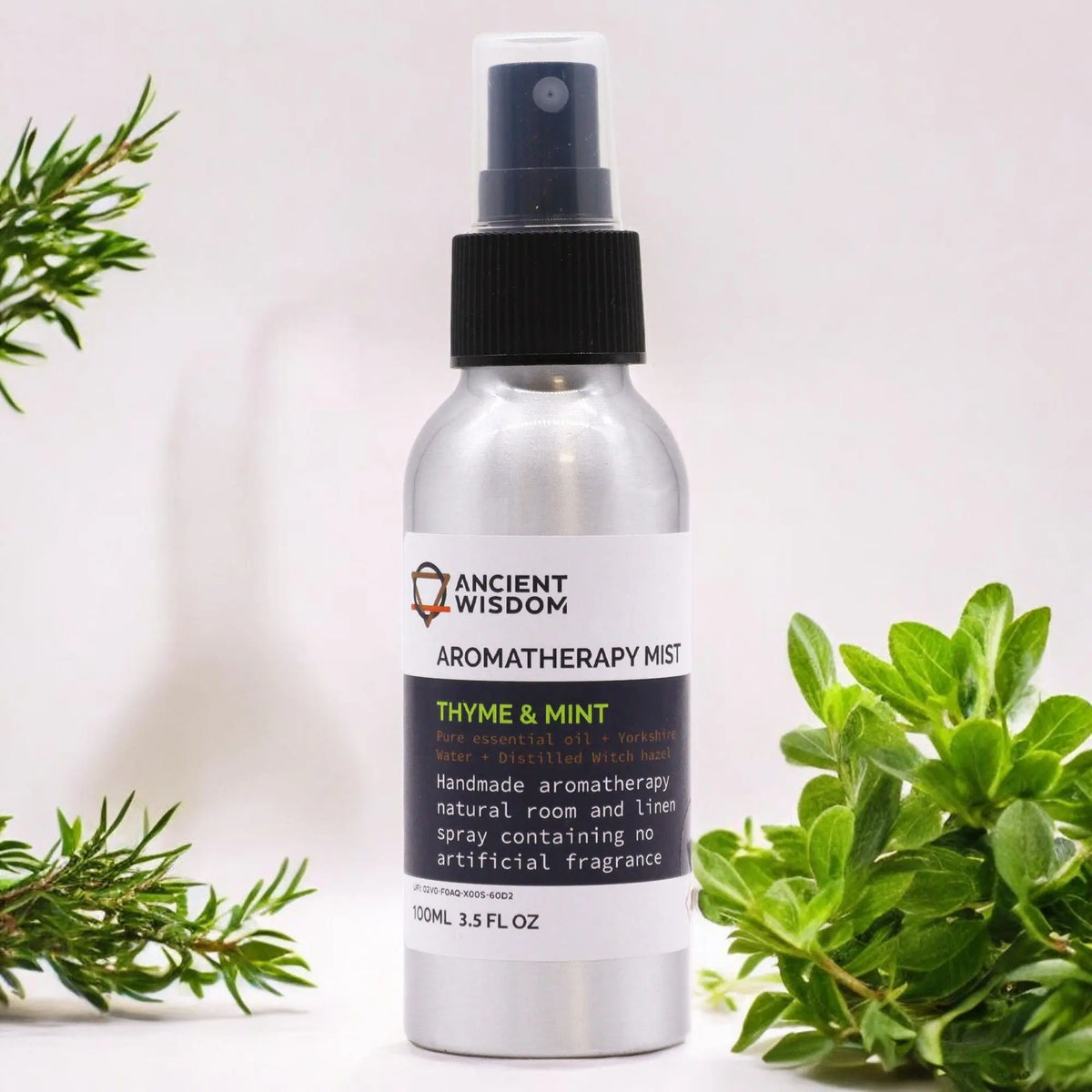 Spray de aromaterapia de 100ml en botella de metal plateado con atomizador negro, rodeado de ramas de tomillo y menta.