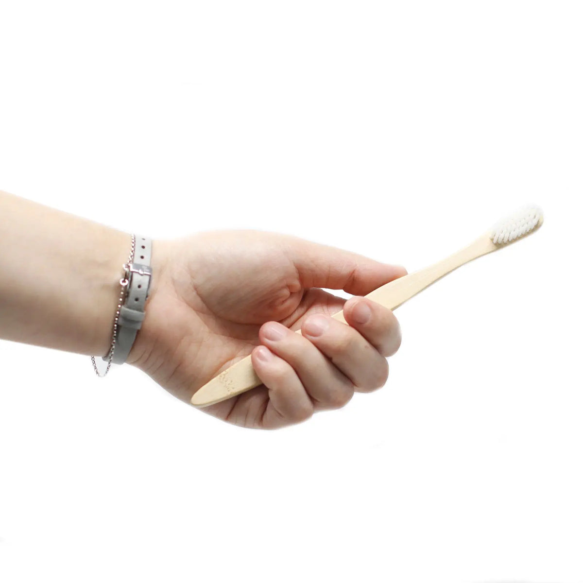 Mano sosteniendo un cepillo de dientes de bambú con mango de madera clara y cerdas de color blanco.