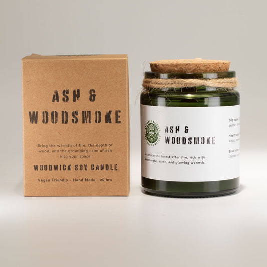 Vela de soja verde con madera, aroma a ceniza y humo de leña, presentada en envase de vidrio y caja kraft.