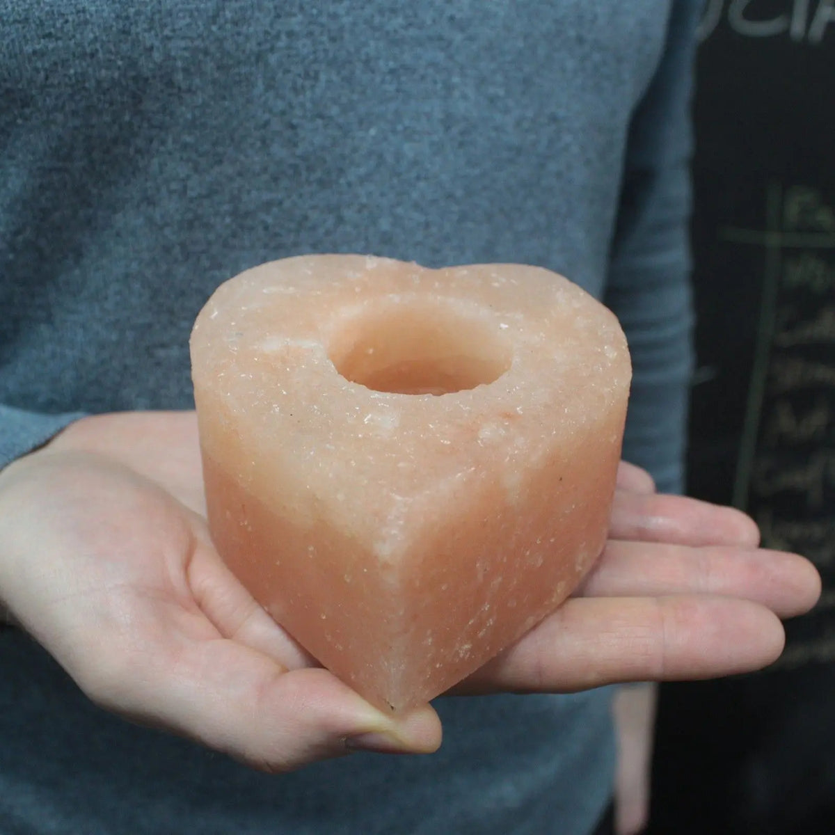 Soporte de vela en forma de corazón hecho de sal del Himalaya de color rosado, sostenido en las manos de una persona.