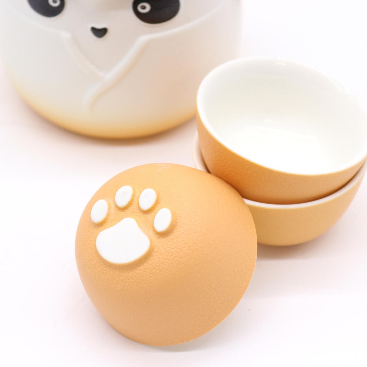Juego de té cerámico con tetera de panda y tazas naranjas con relieve de huella de gato.