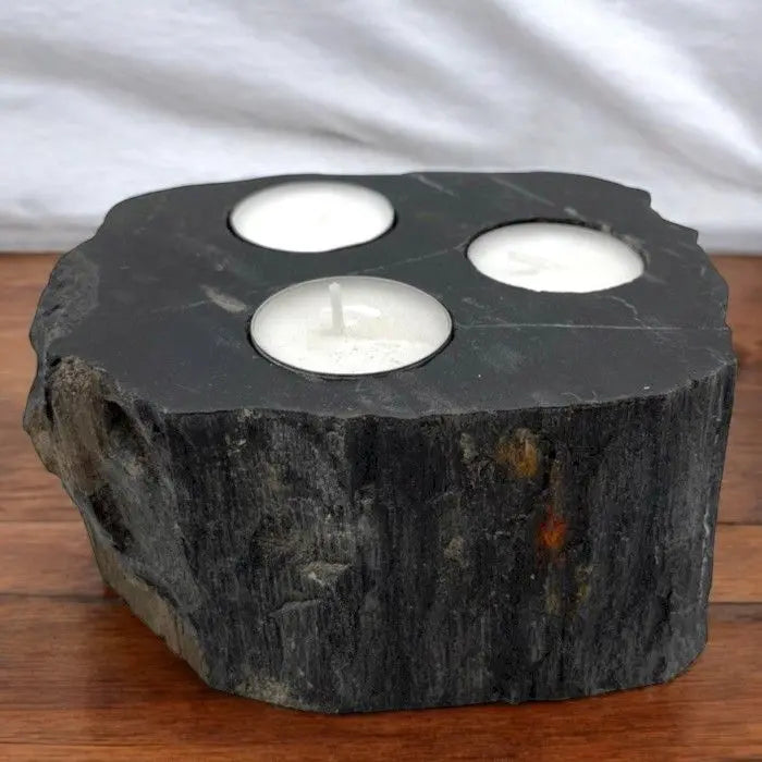 Triple tea light candle holder made from a block of dark, textured petrified wood with natural stone edges.