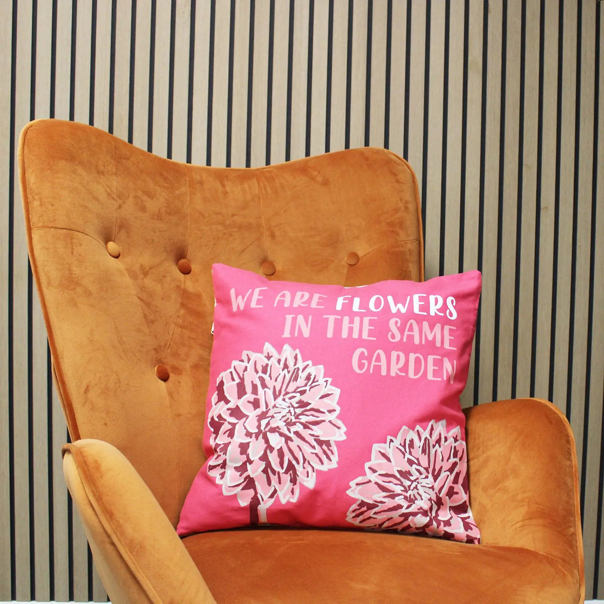 Funda de cojín de algodón rosa con flores y frase en inglés sobre un sillón de terciopelo color ocre.