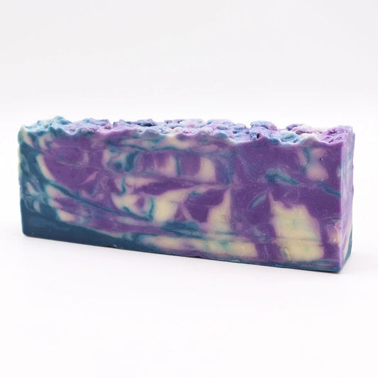 Barra de jabón artesanal con remolinos de colores morado, azul y blanco sobre un fondo blanco limpio y minimalista
